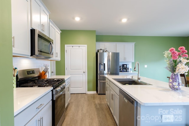 kitchen featuring an island with sink, a sink, light wood-type flooring, white cabinetry, and appliances with stainless steel finishes