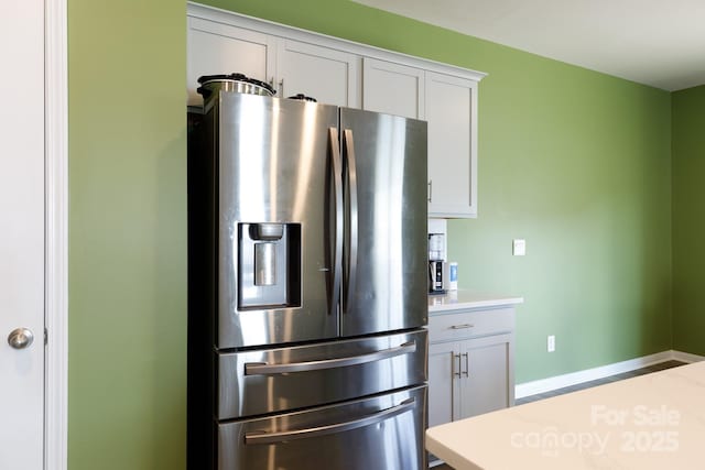 kitchen featuring stainless steel fridge, light countertops, baseboards, and white cabinets