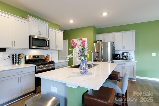 kitchen featuring a sink, a center island with sink, dark wood-type flooring, appliances with stainless steel finishes, and decorative backsplash