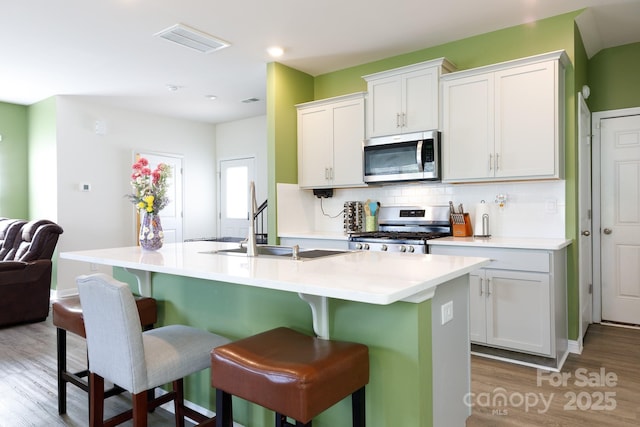 kitchen with light wood-type flooring, a kitchen breakfast bar, decorative backsplash, stainless steel appliances, and an island with sink