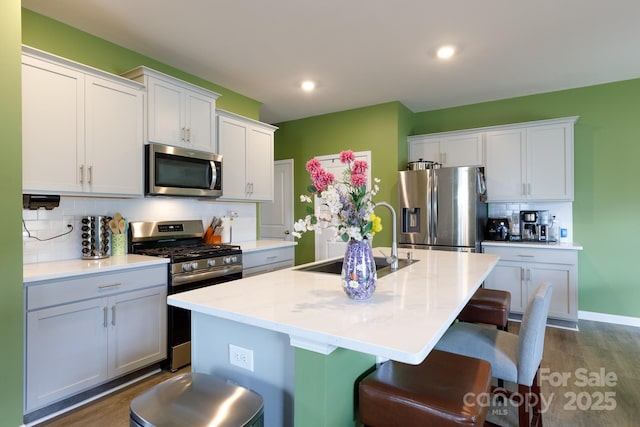 kitchen featuring a sink, stainless steel appliances, dark wood-type flooring, an island with sink, and backsplash