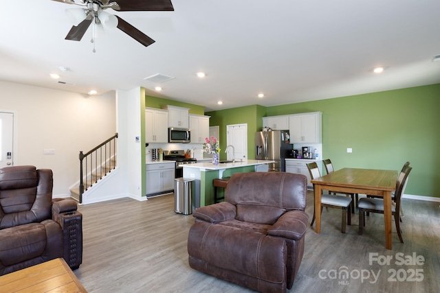 living room with stairway, light wood-style flooring, baseboards, and a ceiling fan
