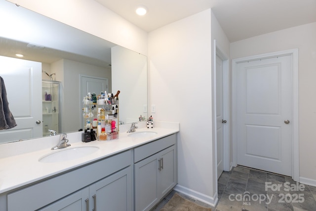 full bath featuring a sink, a stall shower, double vanity, and baseboards