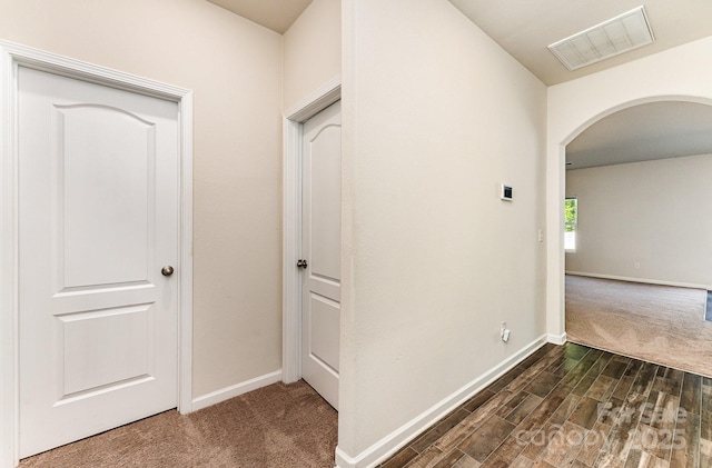 hall featuring arched walkways, baseboards, dark carpet, and visible vents