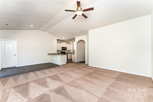 unfurnished living room featuring carpet floors, arched walkways, a ceiling fan, baseboards, and vaulted ceiling