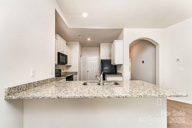 kitchen featuring a peninsula, white cabinetry, arched walkways, a sink, and black appliances
