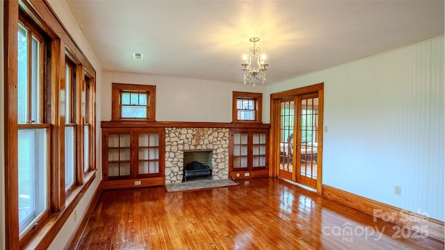 unfurnished living room with visible vents, an inviting chandelier, wood finished floors, a fireplace, and french doors