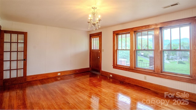 spare room with baseboards, visible vents, wood finished floors, and a notable chandelier