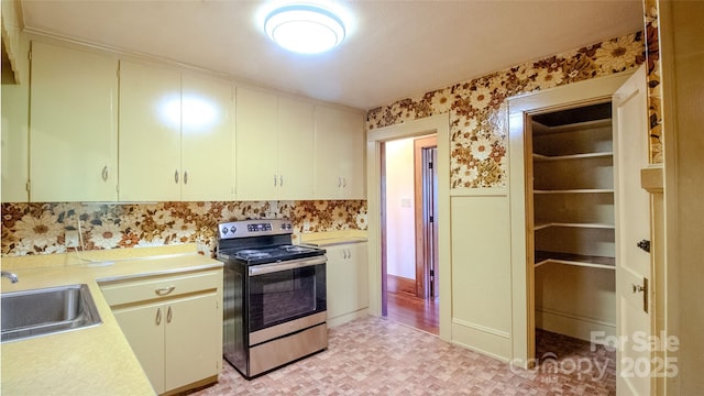 kitchen with stainless steel range with electric stovetop, a sink, light countertops, light floors, and wallpapered walls