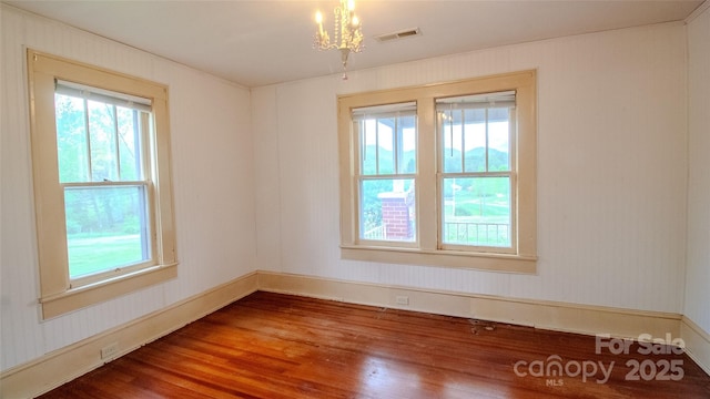 empty room featuring visible vents, wood finished floors, a wealth of natural light, and an inviting chandelier