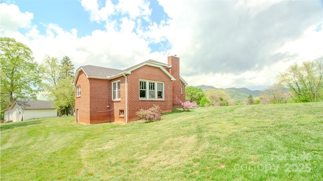 view of side of home featuring a lawn, brick siding, a chimney, and a mountain view