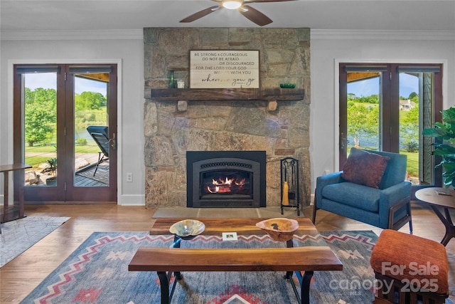living area with ornamental molding, a ceiling fan, a fireplace, wood finished floors, and baseboards