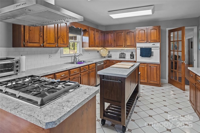 kitchen featuring stainless steel appliances, a sink, exhaust hood, light countertops, and brown cabinets