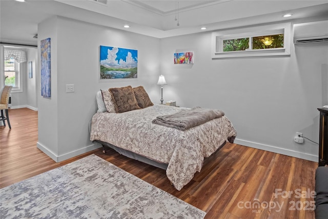 bedroom with an AC wall unit, baseboards, wood finished floors, and recessed lighting