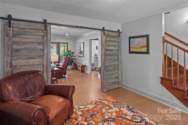 sitting room featuring a barn door, light wood-type flooring, baseboards, crown molding, and stairway