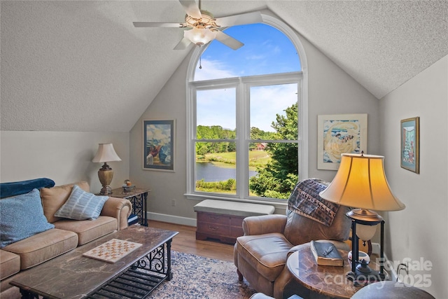 living room featuring a textured ceiling, vaulted ceiling, wood finished floors, baseboards, and ceiling fan