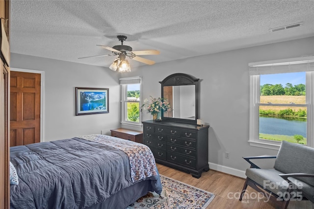 bedroom with multiple windows, wood finished floors, a textured ceiling, ceiling fan, and baseboards