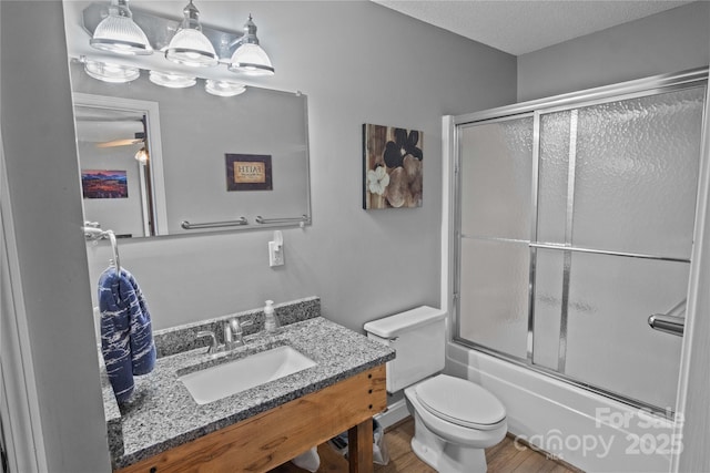 bathroom with wood finished floors, combined bath / shower with glass door, toilet, vanity, and a textured ceiling