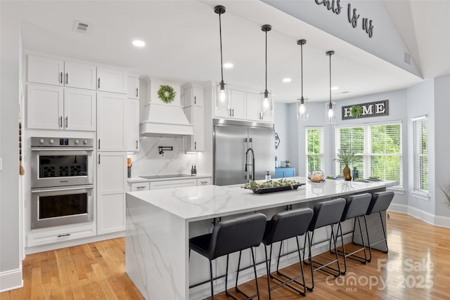 184 Quiet Cove Rd, Mooresville, NC 28117 - kitchen featuring appliances with stainless steel finishes, white cabinets, light wood-style floors, a kitchen island with sink, and custom range hood