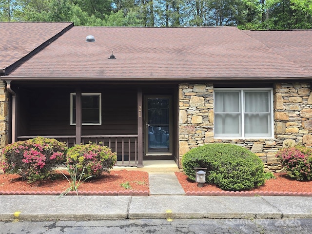 view of front of property featuring a porch, a shingled roof, and stone siding