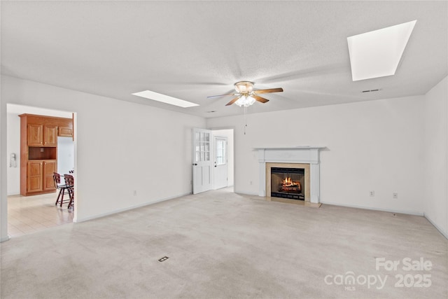 115 Three Oaks Ln, Statesville, NC 28677 - unfurnished living room with a skylight, a ceiling fan, a fireplace with flush hearth, light colored carpet, and baseboards