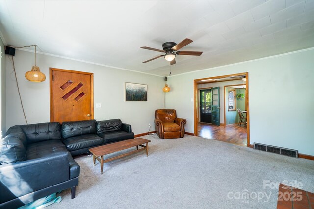 carpeted living room with a ceiling fan, baseboards, and crown molding