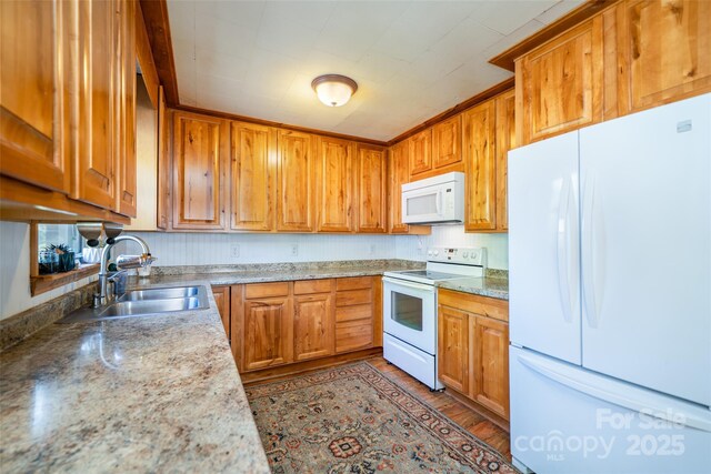 kitchen with white appliances, a sink, wood finished floors, and brown cabinets