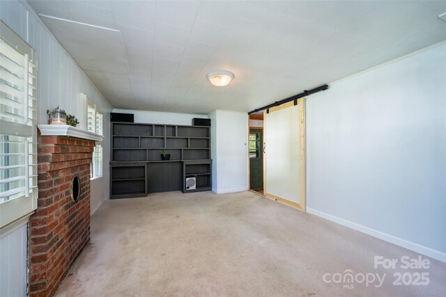 unfurnished living room featuring a barn door, baseboards, carpet floors, and a fireplace