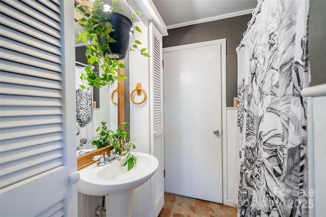 full bath with stone finish flooring, crown molding, and a sink