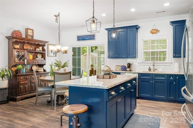 kitchen with blue cabinetry, a sink, light wood-style flooring, decorative backsplash, and healthy amount of natural light