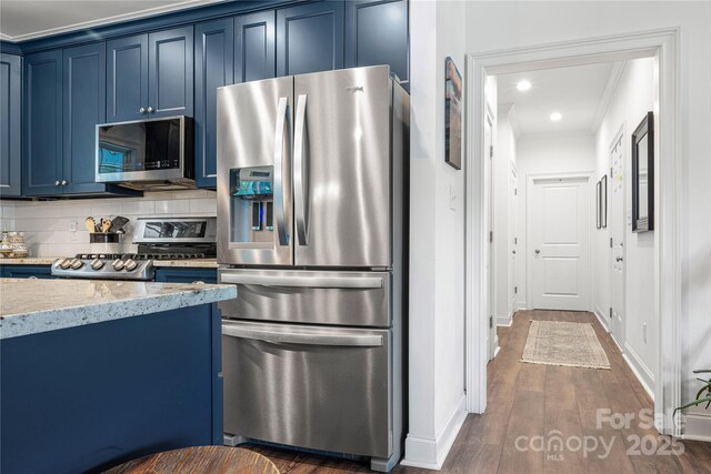 kitchen with appliances with stainless steel finishes, blue cabinetry, crown molding, decorative backsplash, and light stone countertops