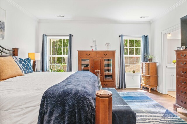 bedroom with ornamental molding, wood finished floors, and ensuite bath