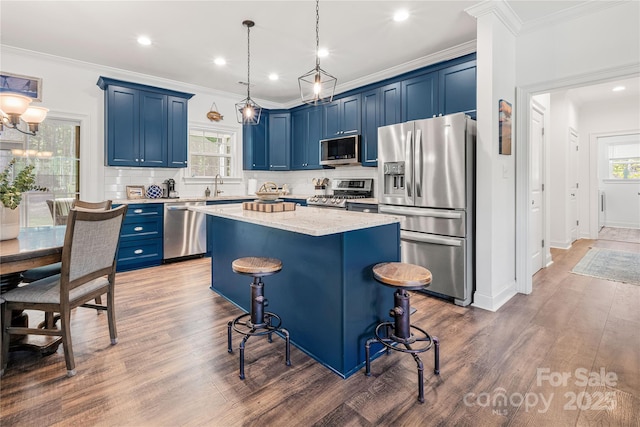 kitchen with appliances with stainless steel finishes, blue cabinetry, a kitchen island, tasteful backsplash, and ornamental molding