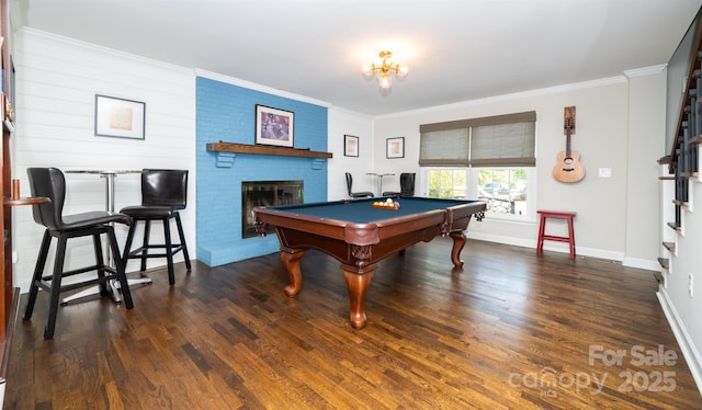 rec room with ornamental molding, a brick fireplace, and wood finished floors