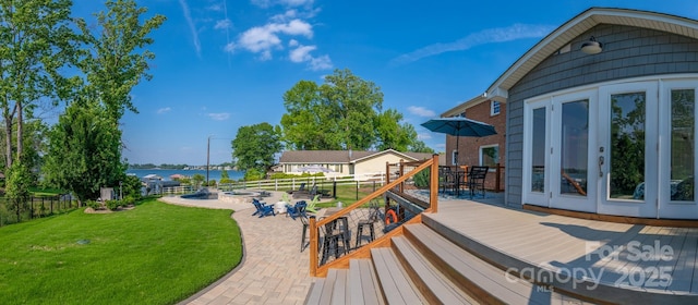 wooden terrace featuring a water view, outdoor dining space, fence, a yard, and a patio area