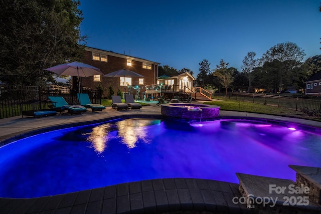 pool at twilight with a fenced backyard, a deck, a patio area, and a pool with connected hot tub
