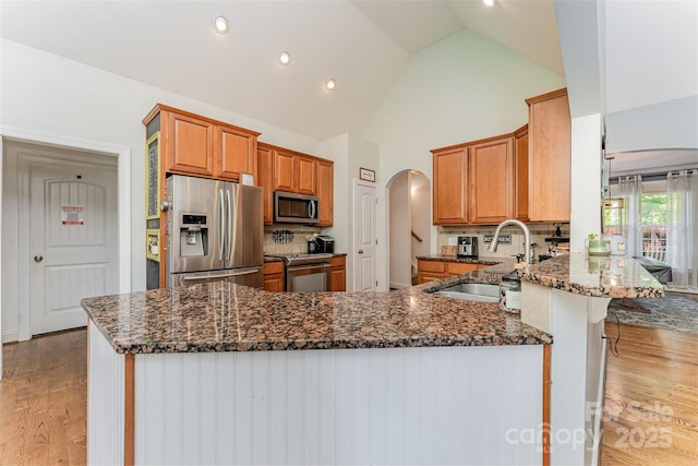 6603 Havencrest Dr, Denver, NC 28037 - kitchen featuring appliances with stainless steel finishes, dark stone countertops, a peninsula, arched walkways, and high vaulted ceiling