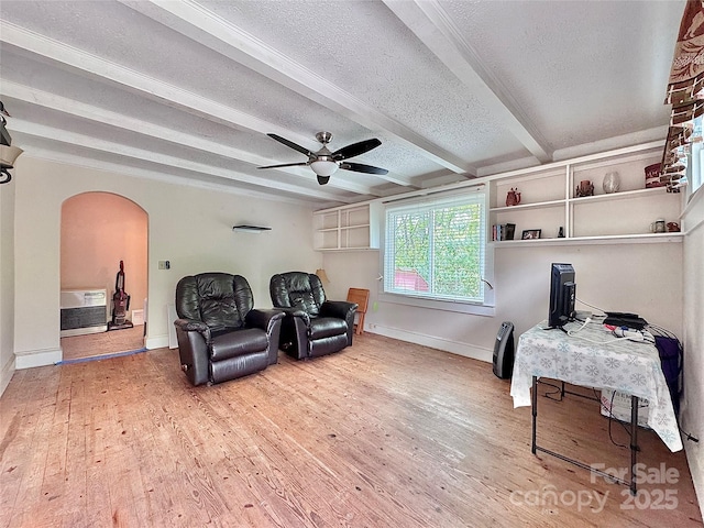 living area with wood finished floors, beam ceiling, a textured ceiling, arched walkways, and a ceiling fan