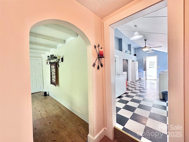 hall with tile patterned floors, baseboards, lofted ceiling, and arched walkways