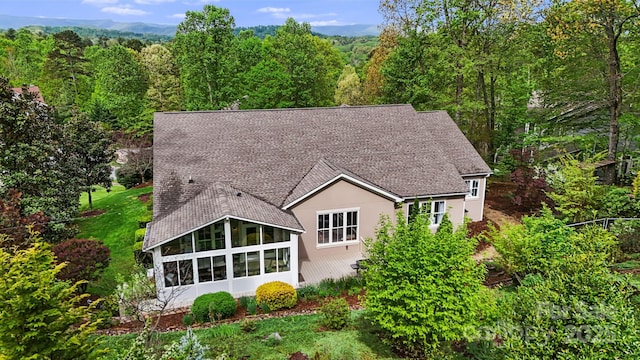 exterior space with roof with shingles, a view of trees, a sunroom, and stucco siding
