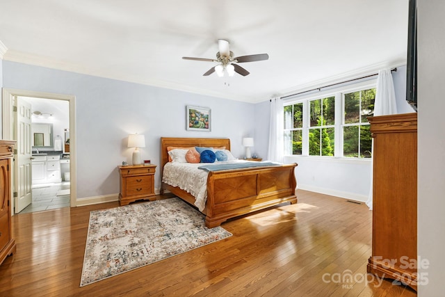bedroom featuring baseboards, ornamental molding, ensuite bathroom, and hardwood / wood-style flooring