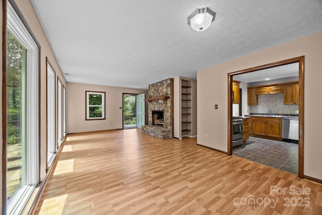 1128 Forest St, Mars Hill, NC 28754 - unfurnished living room featuring light wood-style floors, a sink, a textured ceiling, a stone fireplace, and baseboards