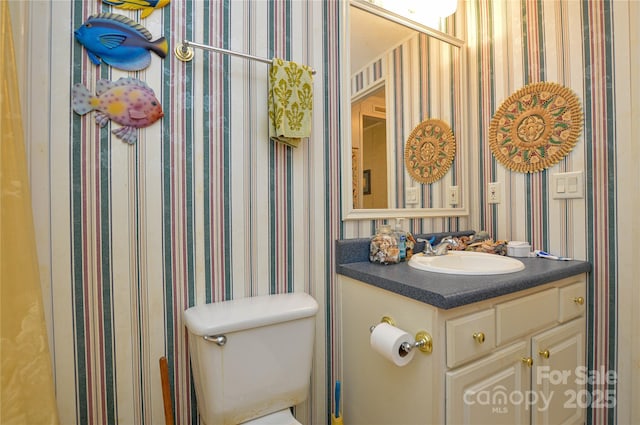 half bathroom featuring wallpapered walls, toilet, and vanity