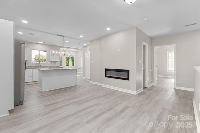 unfurnished living room featuring a glass covered fireplace, baseboards, and light wood-type flooring