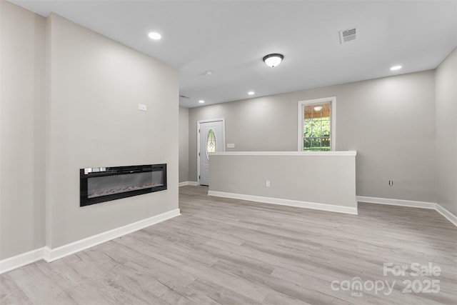 unfurnished living room with baseboards, recessed lighting, a glass covered fireplace, and wood finished floors