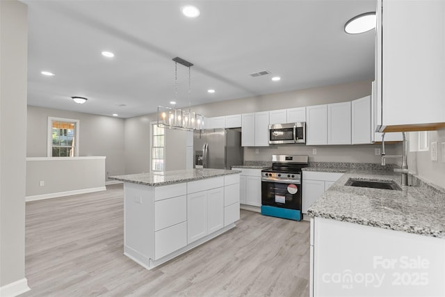 kitchen featuring visible vents, appliances with stainless steel finishes, a center island, a sink, and baseboards
