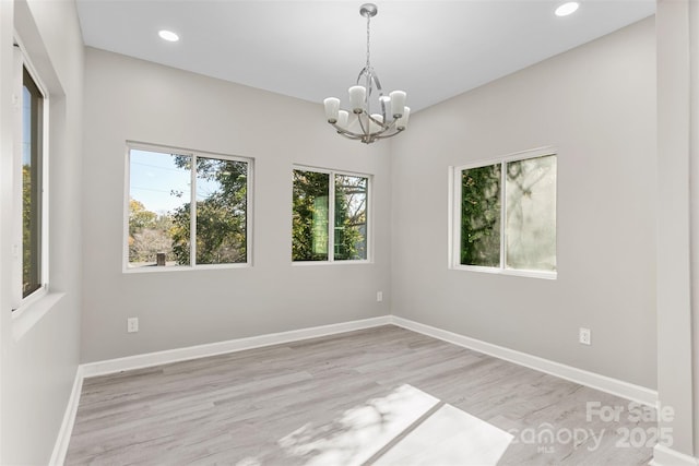 empty room featuring baseboards, recessed lighting, light wood finished floors, and a chandelier