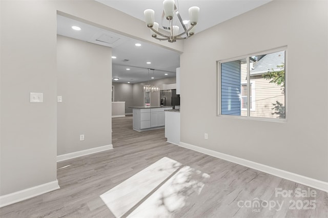 spare room featuring light wood-style floors, recessed lighting, baseboards, and a notable chandelier