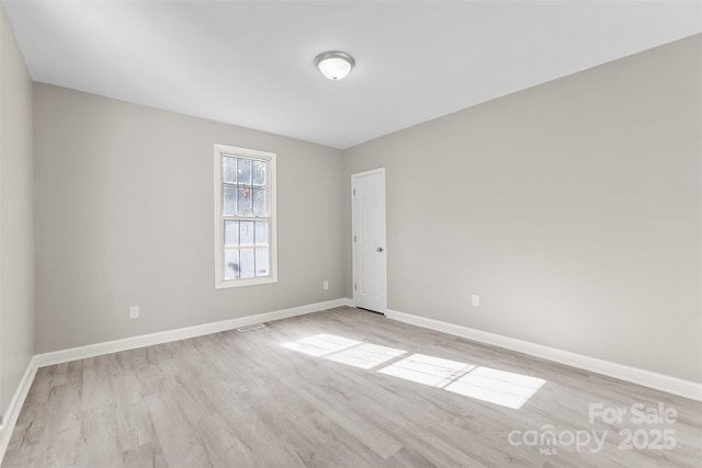 spare room with baseboards, light wood-style flooring, and visible vents