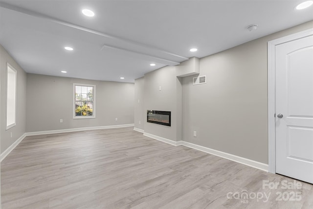unfurnished living room with a glass covered fireplace, recessed lighting, baseboards, light wood-type flooring, and visible vents